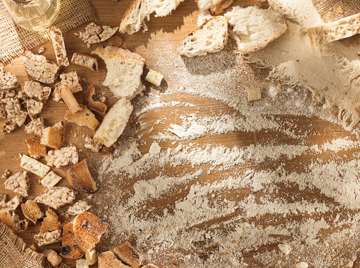 imagem mostra uma mesa de madeira marrom, coberta por diferentes pedaços de pão picado e farinha espalhada por toda a superfície